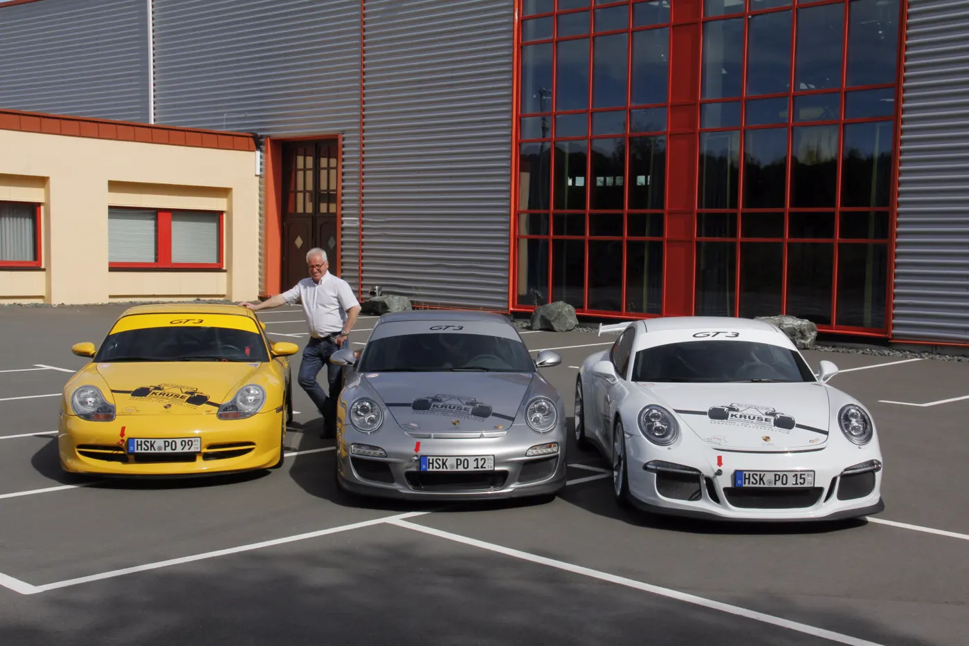 Drei Kruse-Rennwagen — gelb, silber, weiß — in Startaufstellung vor der Halle